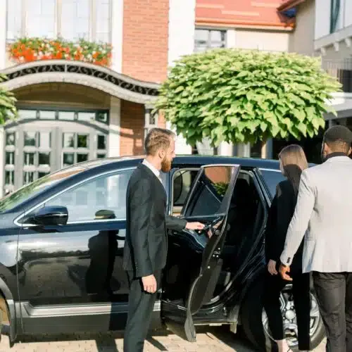 chauffeur-man-opening-car-door-for-business-couple-caucasian-woman-and-african-man-side-view-500x500